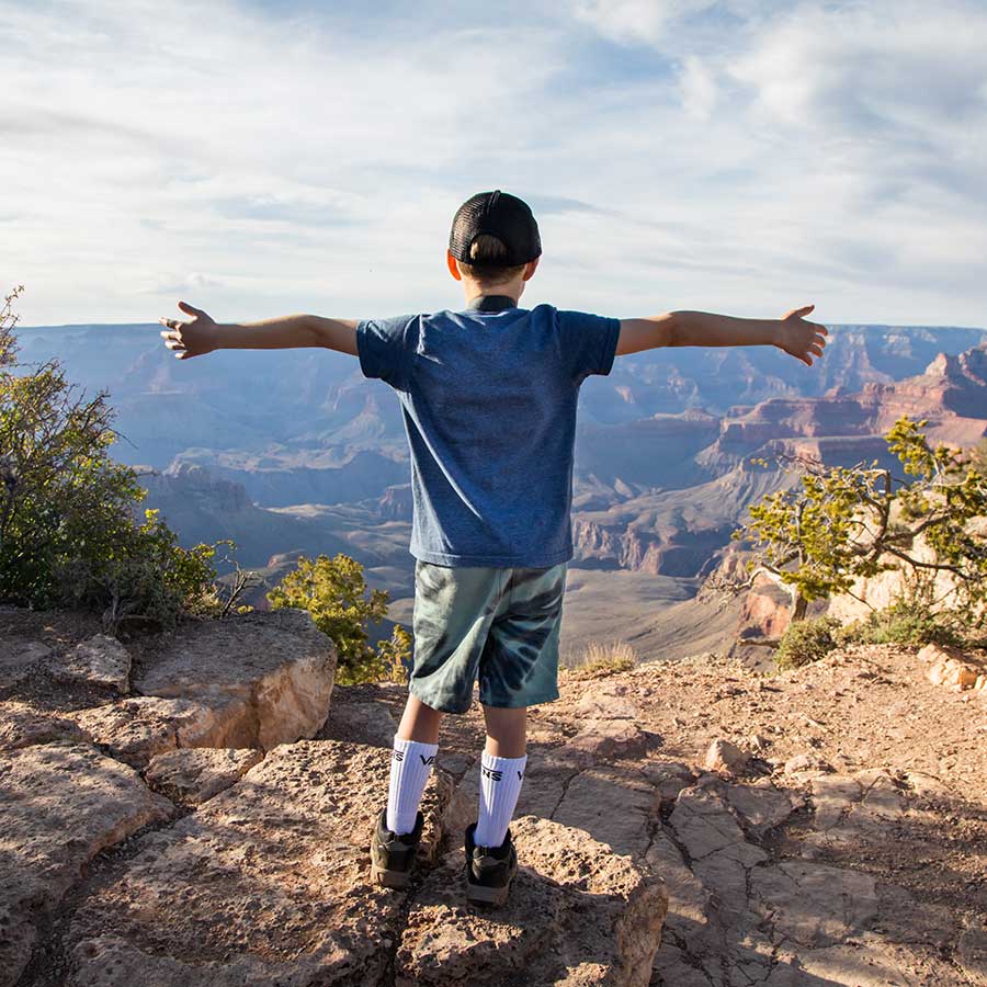 A boy stands with his arms outstretched at the rim of the Grand Canyon.