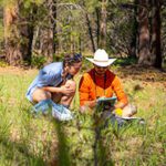 Two volunteers survey a spring in northern Arizona, greenery suggests water nearby